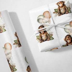 May include: White wrapping paper with a repeating pattern of a monkey holding balloons. The balloons are green, brown, and beige. The text "Isabel" is written on one of the balloons.