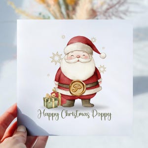 May include: A Christmas card with a watercolour illustration of Santa Claus in a red suit and hat, with a white beard and a gold seal. The card includes the text "Happy Christmas Poppy" and a small gift box.