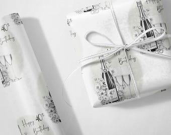 May include: White wrapping paper with a black and white champagne bottle and floral design. The words "Happy 40th Birthday" are printed on the paper. A white ribbon is tied around the wrapped gift.