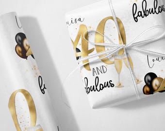 May include: White wrapping paper with gold and black accents. The paper features the number 40 in gold with the text "I am 40 and fabulous". There are black and gold balloons and champagne glasses on the paper.