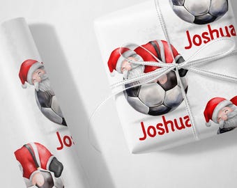 May include: White wrapping paper with a repeating pattern of Santa Claus holding a soccer ball. The paper has the name "Joshua" printed on it in red.