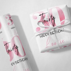 以下が含まれることがあります： ピンクと白の包装紙に、数字の30と「Thirty」と「Happy Birthday」の文字が印刷されています。また、「Louise」という名前も印刷されています。