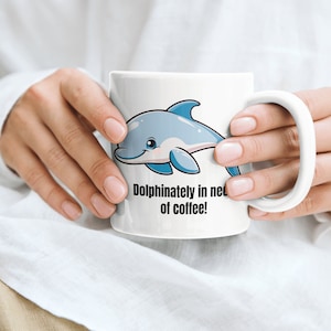 May include: White ceramic mug with a blue cartoon dolphin and the text "Dolphinately in need of coffee!"