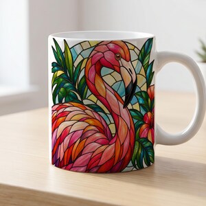 Könnte beinhalten: Ein weißer Keramikbecher mit einer farbenfrohen Illustration im Buntglas-Stil, die einen rosafarbenen Flamingo zeigt. Das Design umfasst üppige grüne Tropenblätter, leuchtend rote Hibiskusblüten und ein geometrisches Hintergrundmuster in Blau und Gelb.
