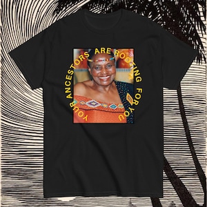 Peut inclure: T-shirt noir avec un graphique circulaire jaune représentant une femme avec un bandeau à perles et le texte "Vos ancêtres vous encouragent".