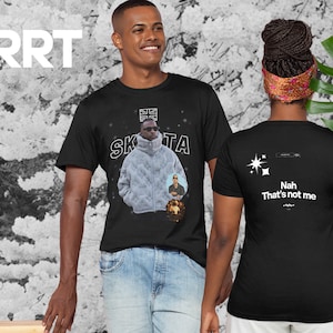 Può includere: Maglietta nera con una stampa grafica di un uomo che indossa una giacca grigia e occhiali da sole. Il testo "SKRTA" è stampato sopra la grafica. La parte posteriore della maglietta ha una grafica bianca di stelle e il testo "Nah That's not me".