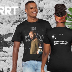 Può includere: T-shirt nere con una grafica di un uomo e il nome "Kano" in bianco. La parte anteriore della maglietta presenta una grafica della bandiera Union Jack. La parte posteriore della maglietta ha il testo "That means I'm direct rudeboy".
