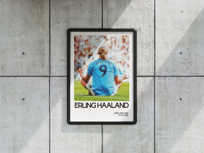 May include: A black and white poster with a photo of a soccer player sitting in a lotus position on a green field. The player is wearing a light blue jersey with the number 9 and the name "HAALAND" on the back. The text "ERLING HAALAND" is printed in black at the bottom of the poster, along with the text "LEEDS, ENGLAND 21 JULY 2000".