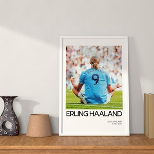 May include: A framed poster featuring a photo of Erling Haaland, a professional soccer player, in a blue jersey with the number 9 on the back. The poster has the text "Erling Haaland" and "Leeds, England 20 July 2000" printed below the photo.