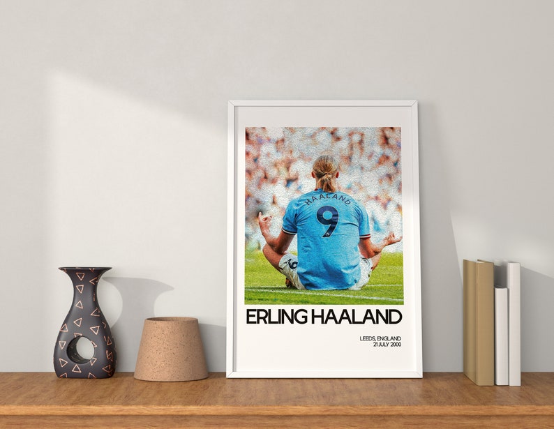 May include: A framed poster featuring a photo of Erling Haaland, a professional soccer player, in a blue jersey with the number 9 on the back. The poster has the text "Erling Haaland" and "Leeds, England 20 July 2000" printed below the photo.