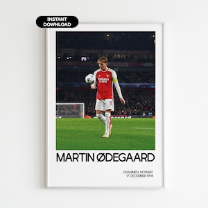 May include: A digital print of a soccer player, Martin Ødegaard, wearing a red and white soccer jersey, holding a soccer ball. The background is a blurry image of a soccer stadium. The text "MARTIN ØDEGAARD" is at the bottom of the print, along with the text "DRAMMEN, NORWAY 17 DECEMBER 1998".