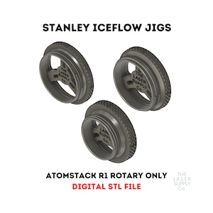 Puede incluir: Tres plantillas de plástico negro impresas en 3D para un accesorio rotatorio Atomstack R1. Las plantillas están etiquetadas con "The Laser Supply Co.". El texto "Atomstack R1 Rotary Only Digital STL File" se muestra debajo de las plantillas.