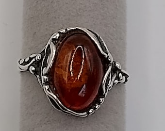 May include: A silver ring with an oval-shaped amber stone set in a detailed, ornate design.
