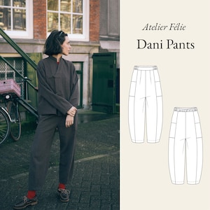 以下が含まれることがあります： 濃い茶色のジャケットとパンツのセットアップを着た女性。赤い靴下と茶色の靴を合わせています。画像には、ピンクのバスケットが付いた自転車と「Atelier Félie Dani Pants」の文字も含まれています。