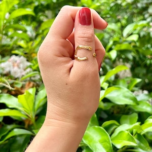 Könnte beinhalten: Ein goldener Ring mit einem einzigartigen, abstrakten Design. Der Ring wird am Daumen einer Hand getragen.