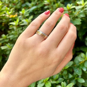 May include: Three thin gold, silver, and rose gold bands stacked on a finger. The bands are all textured.