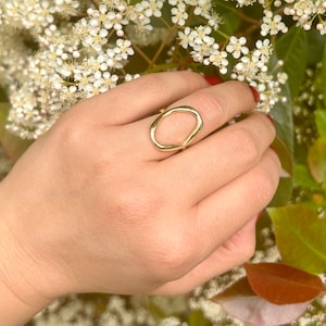 May include: A gold ring with an irregular oval shape. The ring is worn on a hand with white nail polish.