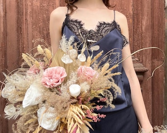 May include: A bouquet of dried flowers and roses in shades of pink, white, and beige. The bouquet is held in front of a navy blue satin top with black lace trim. The background is a weathered, reddish-brown wooden door.