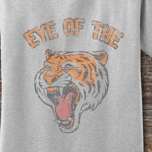 May include: A grey t-shirt with the text "Eye of the" and a vintage illustration of a tiger's face.