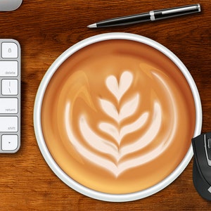 Puede incluir: Una taza de café de cerámica blanca con un diseño de arte latte con un patrón de hojas. La taza está sobre una superficie de madera con un teclado, un bolígrafo y un ratón cerca.