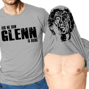 May include: A gray t-shirt with the text "Ask me how Glenn is doing" printed on the front. The shirt is designed to be worn inside out, revealing a black and white image of a man's face.