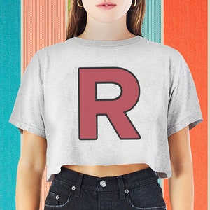 Op de afbeelding: Een grijs gecropped t-shirt met een grote, rode letter "R" bedrukt op de voorkant. De letter heeft een zwarte omtrek.