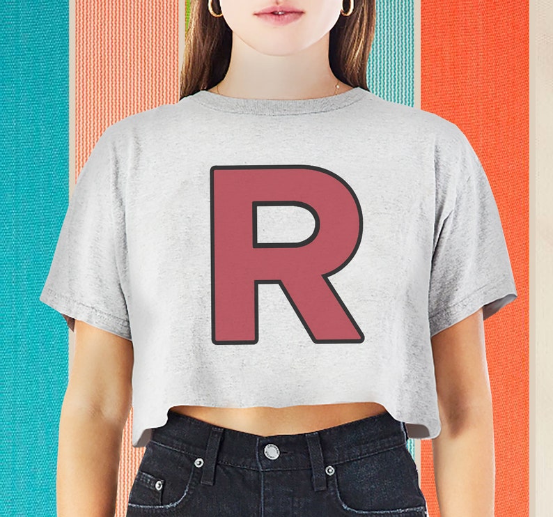 Op de afbeelding: Een grijs gecropped t-shirt met een grote, rode letter "R" bedrukt op de voorkant. De letter heeft een zwarte omtrek.