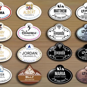 Puede incluir: Una colección de 12 etiquetas de nombre con temática de Disney con varios personajes y ubicaciones. Las etiquetas de nombre son de forma ovalada con fondo blanco y texto negro. Algunas de las etiquetas de nombre tienen un borde dorado y otras tienen un borde negro. Las etiquetas de nombre presentan personajes como Mickey Mouse, Tinkerbell y Darth Vader. Las etiquetas de nombre también presentan ubicaciones como Disneyland, Disney World y Star Wars.