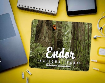 May include: A mousepad featuring a stylized illustration of a forest with tall trees and the text "Endor National Park. The Enchanted Sanctuary Moon."