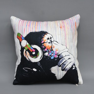 Peut inclure: Un coussin décoratif avec un imprimé graphique coloré d'un gorille portant des écouteurs. L'arrière-plan est une toile blanche avec des lignes verticales colorées.