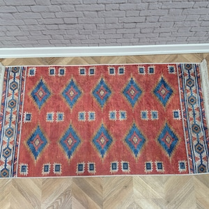 May include: A red, blue, and cream colored rug with a geometric pattern. The rug has fringe on all four sides.