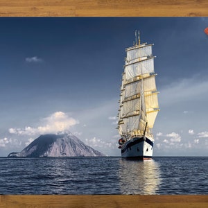 Könnte beinhalten: Ein weißes Segelboot mit vollen Segeln, das an einer kleinen, felsigen Insel mit einem wolkenbedeckten Gipfel vorbeifährt. Das Meer ist tiefblau und der Himmel ist strahlend blau mit weißen Wolken.