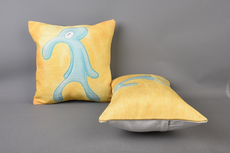 May include: Two decorative throw pillows. One pillow is yellow with a blue figure of a person with a long nose. The other pillow is yellow.
