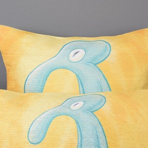 May include: Two yellow throw pillows with a blue abstract design. The pillows are stacked on top of each other.