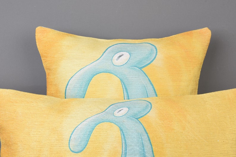May include: Two yellow throw pillows with a blue abstract design. The pillows are stacked on top of each other.