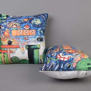 Op de afbeelding: Twee decoratieve kussens met een blauw, groen en oranje pixelontwerp ge&iuml;nspireerd op het videospel Super Mario Bros. De kussens hebben een sterrenhemel als achtergrond en de tekst "???".