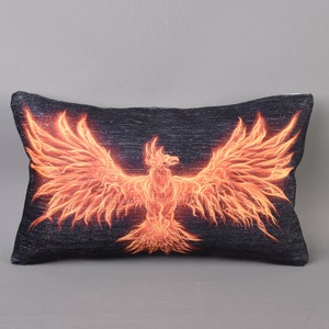 May include: Rectangular pillow with a dark background and a fiery orange phoenix design. The phoenix is depicted with outstretched wings, creating a striking contrast against the dark fabric. The pillow is a decorative home accent.