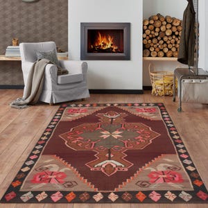 Könnte beinhalten: Ein rechteckiger Teppich mit einem geometrischen Muster in Braun-, Rosa- und Grautönen. Der Teppich hat ein zentrales Medaillon-Design und einen Rand mit Blumen- und Diamantmotiven. Er liegt auf einem Holzboden.