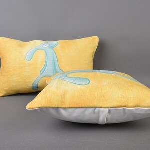 May include: Two yellow throw pillows with a blue and green cartoon character printed on them. The pillows are made of a soft, textured fabric.