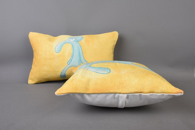 May include: Two yellow throw pillows with a blue and green cartoon character printed on them. The pillows are made of a soft, textured fabric.
