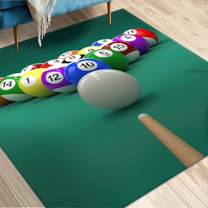 May include: A green rectangular rug with a pool table design. The rug features a cue stick and a rack of numbered billiard balls in various colors, including red, yellow, and blue. The cue ball is white.