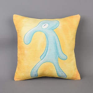 May include: A yellow throw pillow with a blue, cartoon-like figure of a person with a long nose and arms. The figure is standing on the pillow.