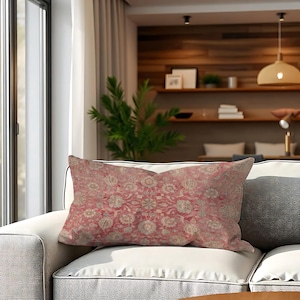 May include: A rectangular cushion featuring a floral design in red, beige, and cream tones. It rests on a white sofa, with a grey cushion to the right. The cushion's pattern has a vintage or antique style, suitable for home decor.