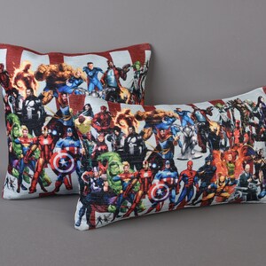 May include: Two decorative throw pillows with a white background and a colorful print of various superheroes. The pillows are rectangular and have a red and white striped border.
