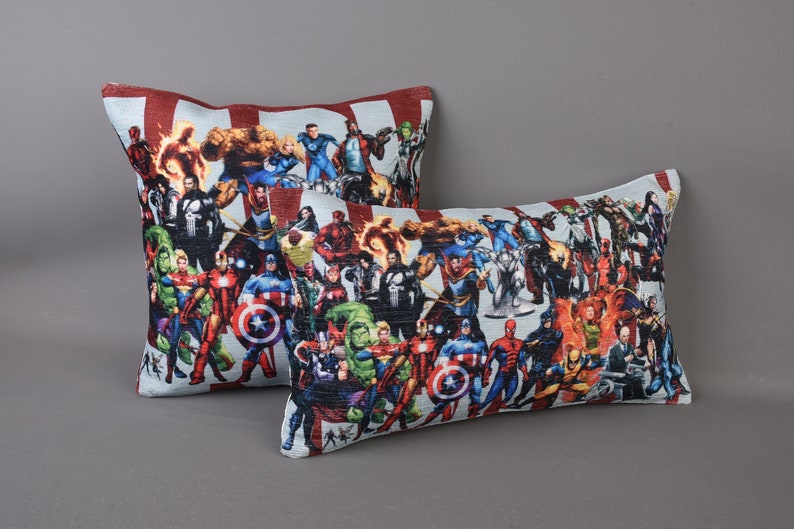 May include: Two decorative throw pillows with a white background and a colorful print of various superheroes. The pillows are rectangular and have a red and white striped border.