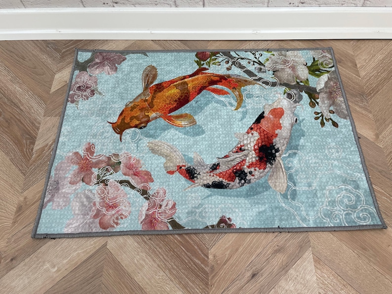 May include: A blue and white rug with a floral design and two koi fish. The fish are orange and red with black markings. The rug has a gray border.