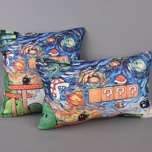 Op de afbeelding: Twee decoratieve kussens met een blauwe, groene, oranje en gele print met een videogamethema. De kussens hebben een Starry Night-achtige achtergrond met vraagtekens en andere videogame-symbolen.