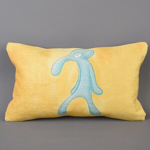 May include: A yellow pillow with a blue cartoon character printed on it. The character has a long nose and is standing with its arms at its sides.