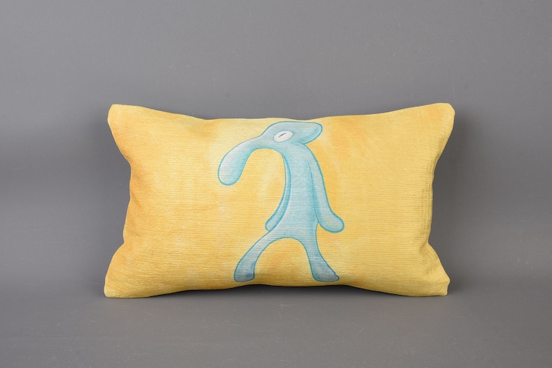 May include: A yellow pillow with a blue cartoon character printed on it. The character has a long nose and is standing with its arms at its sides.