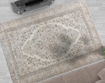 May include: A beige area rug with a detailed floral pattern in shades of brown and grey. The rug has a border with a repeating geometric design.